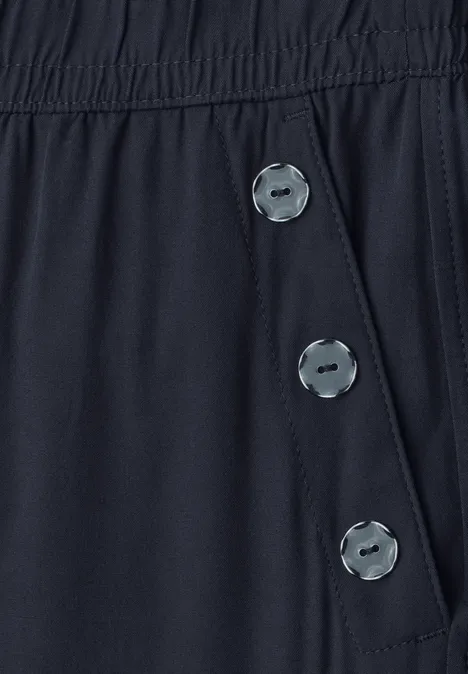 Nahaufnahme eines dunkelblauen Kleidungsstücks mit elastischem Bund und drei silbernen Knöpfen an der Seite.