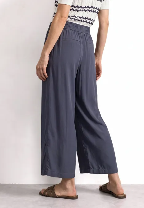 Femme portant un pantalon large bleu marine 7/8 à taille élastique et poches, avec haut rayé et sandales.