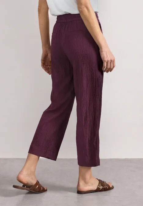 Mid Waist Wide Leg Hose im Loose Fit rustic rouge Rückansicht einer Person mit purpurfarbenen Plisseehosen und braunen Sandalen.
