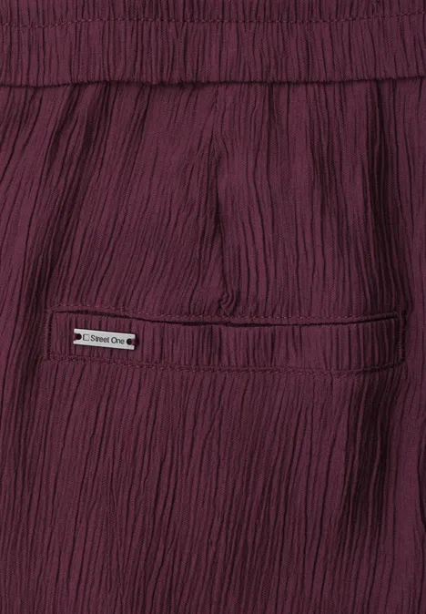Mid Waist Wide Leg Hose im Loose Fit rustic rouge Nahaufnahme einer weinroten, plissierten Hose mit Gesäßtasche und kleinem Metall-Emblem