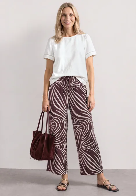 Persoon met wit T-shirt, wijde broek met zebraprint, sandalen en een bruine tas.
