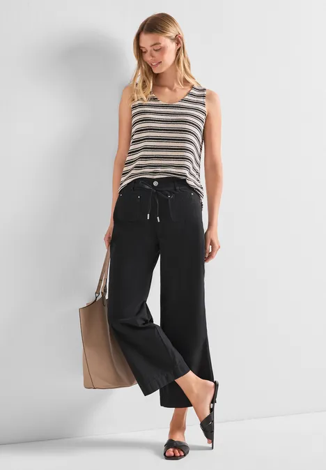 Frau in gestreiftem Top und weiten schwarzen Hosen, trägt Tasche und flache Schuhe.