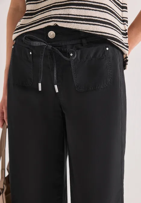 Person trägt gestreiftes Oberteil und schwarze, lässige Hose mit Tunnelzugbund und aufgesetzten Taschen.