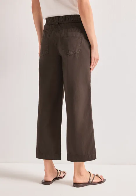 Modell trägt braune, weite, knöchellange Hose mit elastischem Bund und flachen schwarzen Sandalen.