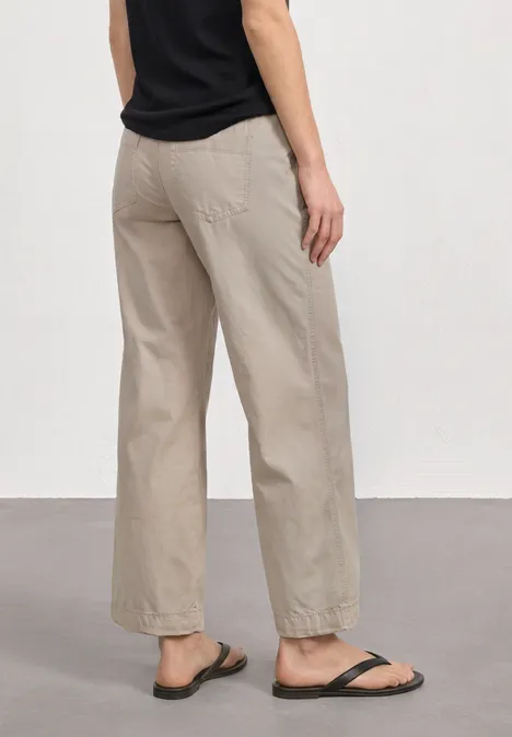 Straight Leg Hose in Washed-Optik sepia sand Person von hinten in beigen, weiten Hosen, schwarzem Oberteil und schwarzen Sandalen vor neutralem Hintergrund.