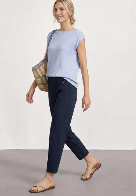 Vrouw in lichtblauw topje, donkerblauwe broek, platte sandalen en een rieten tas.