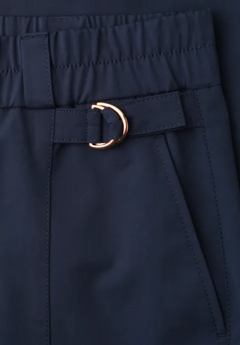 Close-up van een donkerblauw kledingstuk met elastische taille, zijzak en gouden D-ring