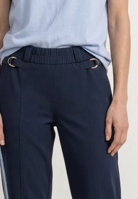 Donkerblauwe broek met elastische taille en zilverkleurige ringen, gecombineerd met lichtblauw shirt.