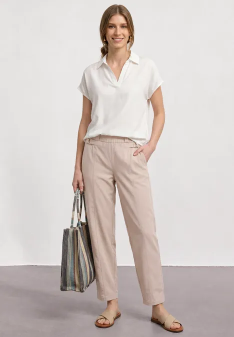 Iemand draagt een wit overhemd met korte mouwen, een beige broek, sandalen en een grote gestreepte tas.