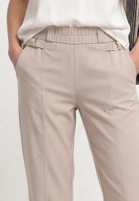 Lichtbeige broek met elastische taille en steekzakken, gedragen door model.
