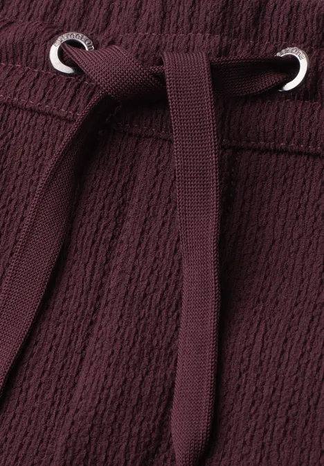 Korte broek met structuur in Loose Fit rustic rouge Close-up van bordeaux stof met aantrekkoord en metalen oogjes.