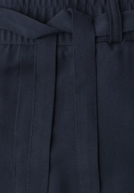 Close-up van een donkerblauwe broek met elastische taille en los gestrikte stoffen ceintuur.
