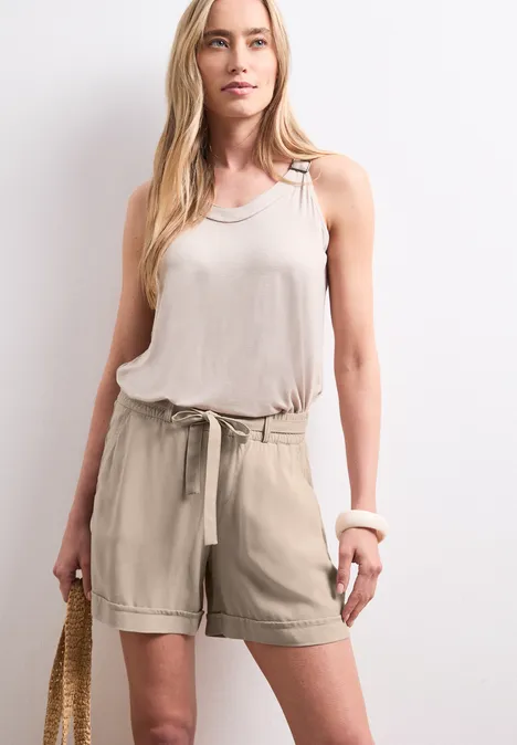 Vrouw in beige tanktop en short met een strozak voor een lichte achtergrond.