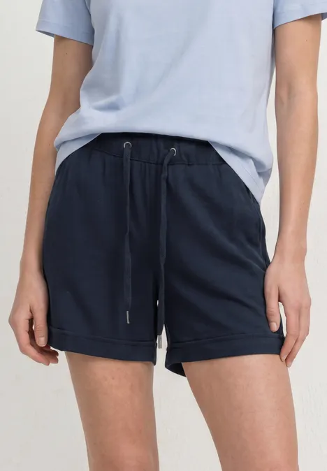 Eine Person trägt ein hellblaues T-Shirt und dunkelblaue Shorts mit Tunnelzug.