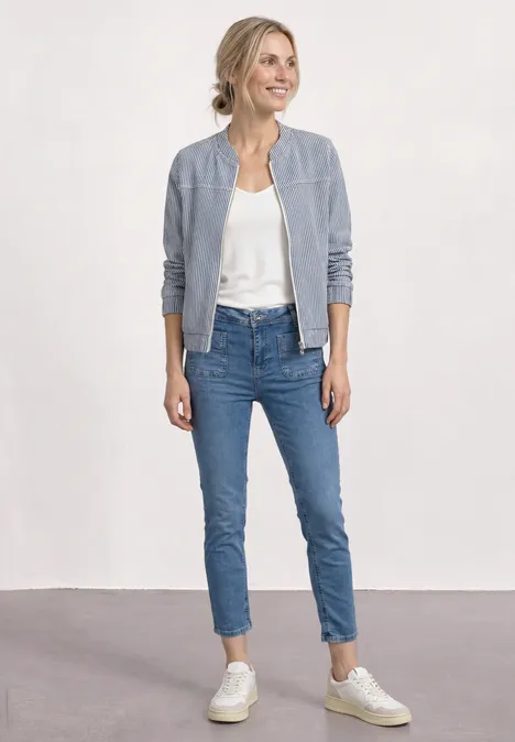 Straight Leg Jeans mit aufgesetzten Taschen Medium Blue Random Wash Eine Frau in Jeans, weißem Top, grauer Bomberjacke und hellen Sneakern steht vor neutralem Hintergrund.
