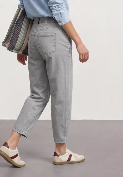 High Waist Barrel Leg Jeans im Loose Fit Light Grey Random Eine Person trägt hellgraue Jeans, weiße Sneaker mit dunklen Streifen und eine gestreifte Umhängetasche.