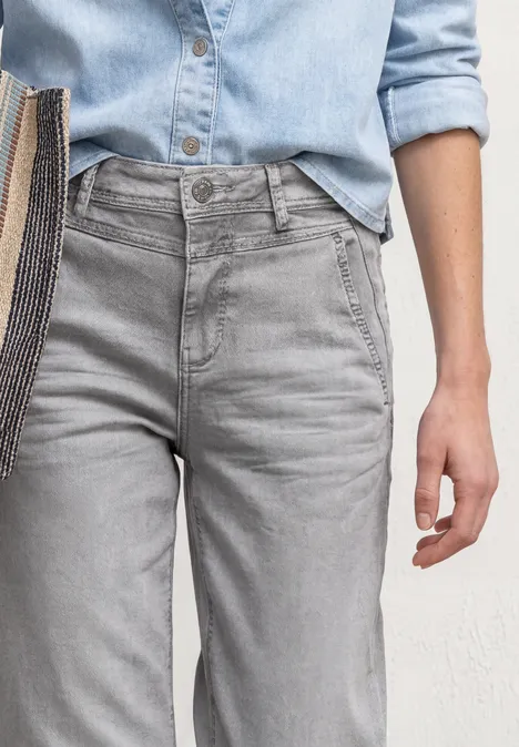 High Waist Barrel Leg Jeans im Loose Fit Light Grey Random Hohe graue Jeans und hellblaues Jeanshemd, Torso mit Hand und Schultertasche zu sehen.