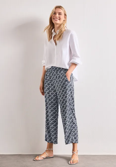 High Waist Wide Leg Hose im Loose Fit shadowed navy Frau in weißer Bluse, karierter, weit geschnittener Hose und flachen Sandalen steht vor hellem Hintergrund.
