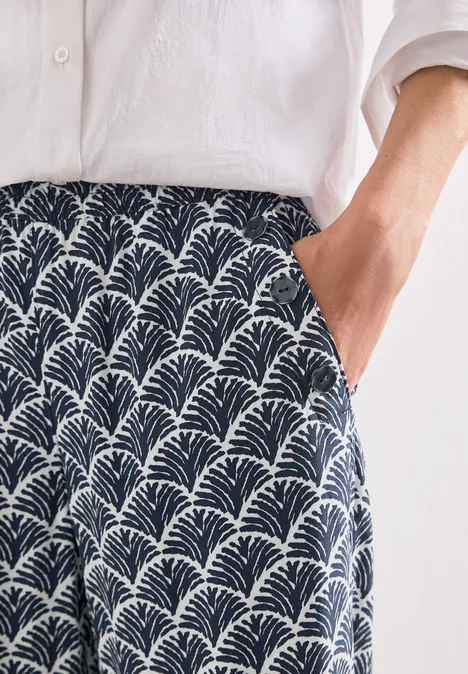 High Waist Wide Leg Hose im Loose Fit shadowed navy Weißes Leinenhemd und marineblaue Culotte mit weißem Fächer-Print, Hand in der Tasche.