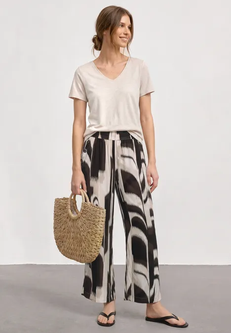 High Waist Wide Leg Hose im Loose Fit espresso brown Frau in lockerem weißen T-Shirt, weiten gemusterten Hosen, schwarzen Flip-Flops und Strohtasche.