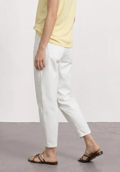 High Waist Barrel Leg Jeans im Loose Fit Off White washed Seitliche Ansicht einer Person in weißer Hose, gelbem Top und schwarzen Sandalen vor neutralem Hintergrund.