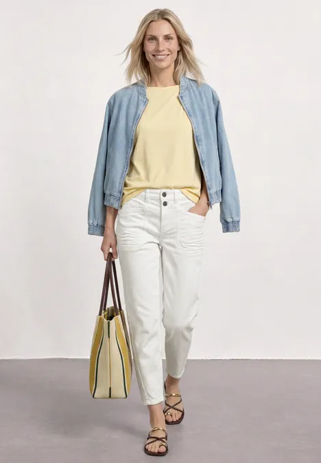 High Waist Barrel Leg Jeans im Loose Fit Off White washed Frau im lässigen Outfit: hellblaues Jackett, gelbes Shirt, weiße Hose, Sandalen und gelbe Tasche.