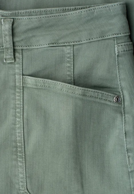 Nahaufnahme einer grünlichen Stoffhose mit sichtbarer Fronttasche, Naht und Gürtelschlaufe.
