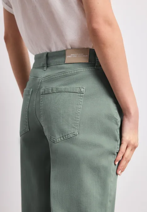 Rückansicht einer Person in hellgrünen Jeans, Händen am Oberschenkel.