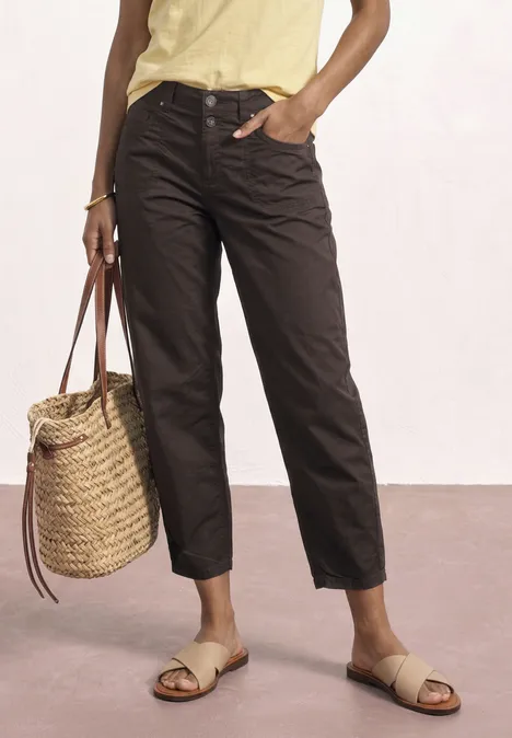 High Waist Barrel Leg Hose espresso brown Frau trägt braune Hose, gelbes Top, geflochtene Handtasche und Sandalen.