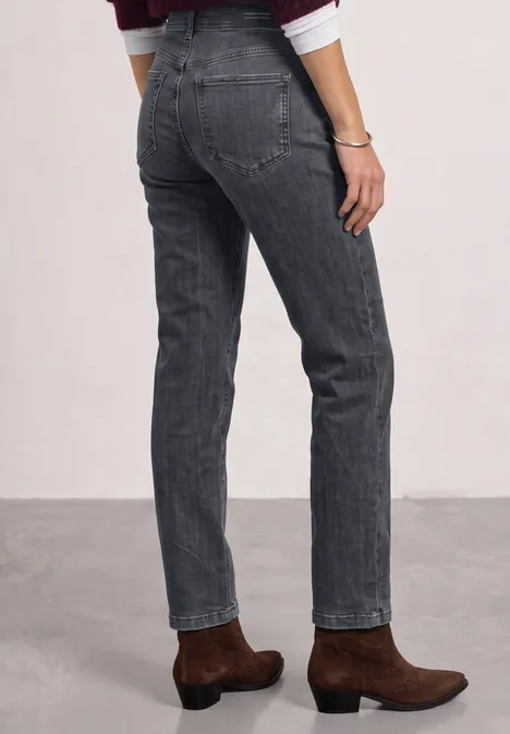 Persoon draagt grijze rechte jeans en bruine enkellaarsjes tegen een neutrale achtergrond.