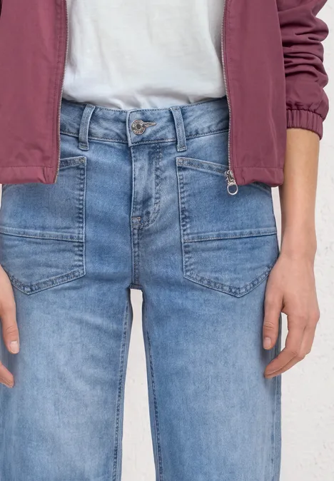 Mid Waist Wide Leg Jeans im Loose Fit Light Blue Random washed Person trägt helle Jeans, weißes Shirt und rote Jacke, nur Oberkörper und Hände sichtbar.
