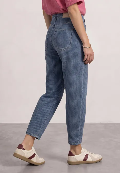 Zijaanzicht van iemand in blauwe jeans en witte sneakers met bordeaux strepen.