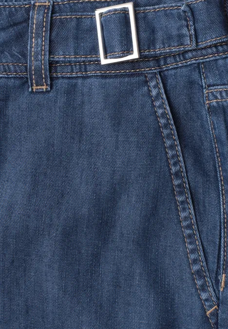 Close-up van een blauwe spijkerbroek met riemlussen, metalen gesp en zichtbare naden.