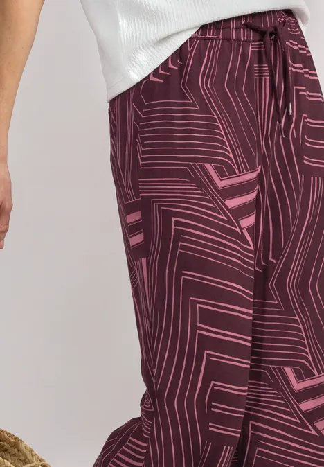 Une personne porte un haut blanc et un pantalon bordeaux à motif géométrique rose.