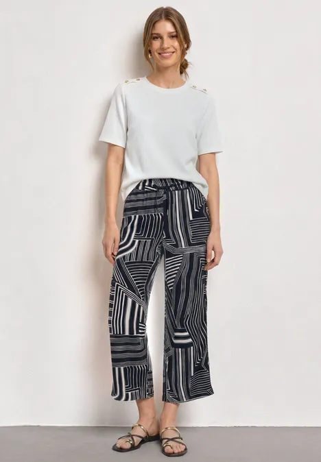 Vrouw met een wit T-shirt en zwarte, wijdvallende broek met patronen en sandalen