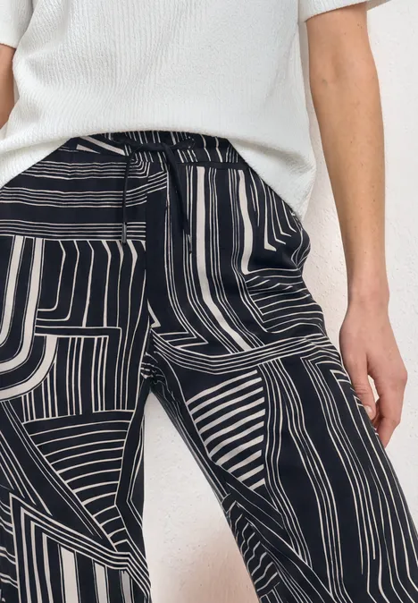 Persoon draagt een wit truitje en een zwart-witte broek met abstract streepdessin.