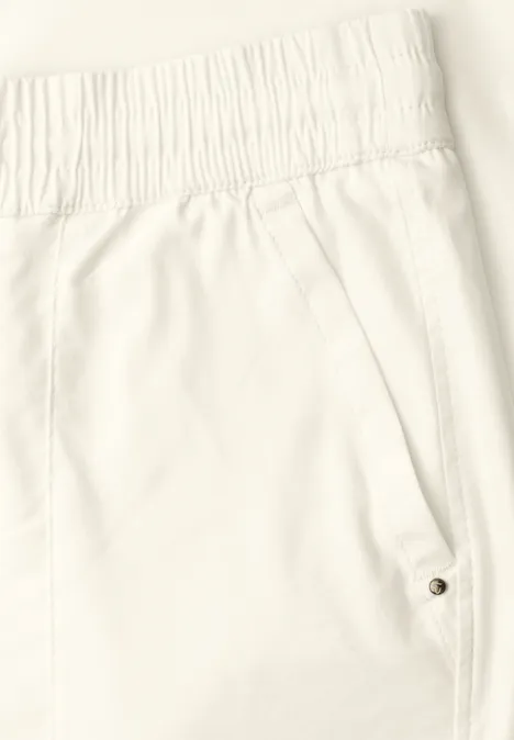 Close-up van een witte broek met elastische taille en zijzak met drukknoop.