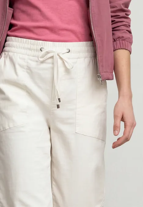 Een persoon draagt een roze jas, een fuchsia top en een lichte, losse broek met aantrekkoord.