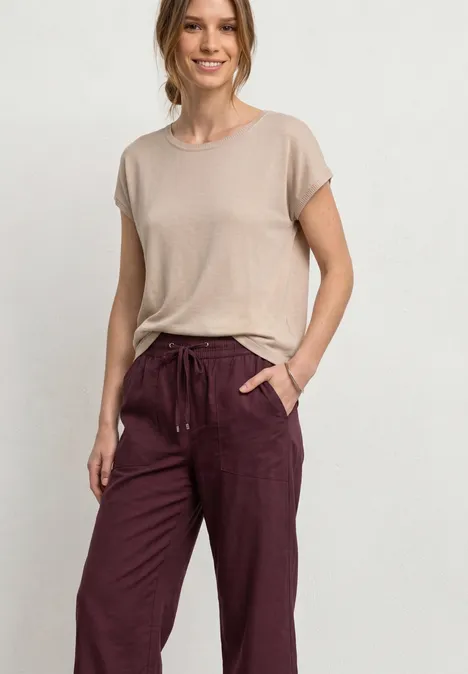 Broek met Straight Leg pijpen in casual pasvorm en omgeslagen boorden rustic rouge Een vrouw lacht in een lichte studio, gekleed in een beige top en bordeauxrode broek met trekkoord.