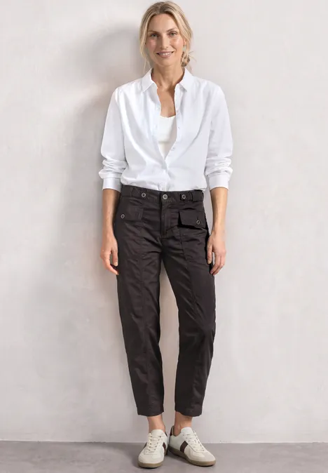 High Waist Barrel Leg Hose im Casual Fit black coffee Person mit weißem Hemd, schwarzen Hosen und weißen Sneakern vor neutralem Hintergrund.