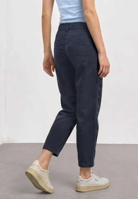 High Waist Barrel Leg Hose im Casual Fit darkest blue Seitliche Rückansicht: Person trägt hochgeschnittene, schwarze Jeans und weiße Sneaker vor hellem Hintergrund.