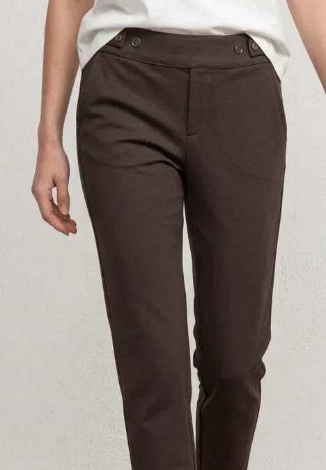 Bruine damesbroek met smalle pasvorm, hoge taille en knoopdetails aan de zijkant.