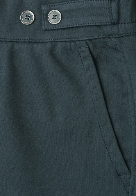 Close-up van een donkere broek met schuine zak en twee sierknopen in de taille.