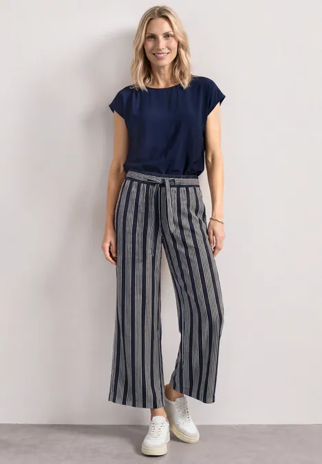 Mid Waist Wide Leg Hose mit Streifen darkest blue Eine Frau trägt ein dunkelblaues T-Shirt, gestreifte Culotte-Hosen und weiße Sneaker vor hellem Hintergrund.