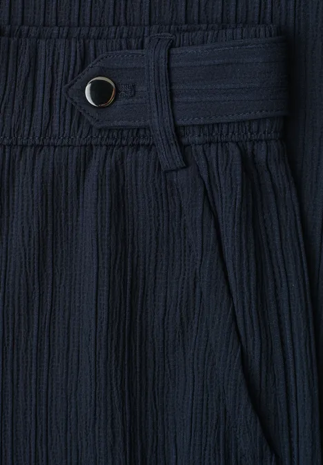 Detailaufnahme eines dunkelblauen, plissierten Stoffs mit Bund, Gürtelschlaufe und Druckknopf.