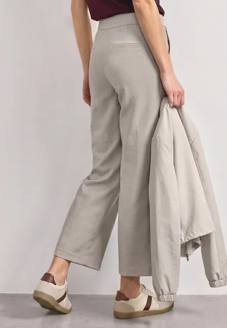 Model draagt wijde grijze broek, houdt bijpassend colbert vast en combineert dit met plateau-sneakers.