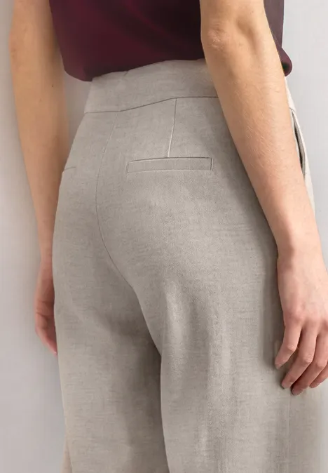 Achteraanzicht van een persoon in strak gesneden, lichtgrijze pantalon met tailleband.
