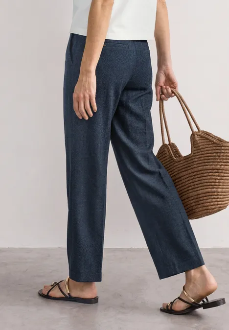 High Waist Jerseybroek met casual pasvorm darkest blue Vrouw in donkerblauwe broek, wit shirt, platte sandalen en met een gevlochten strooien tas.