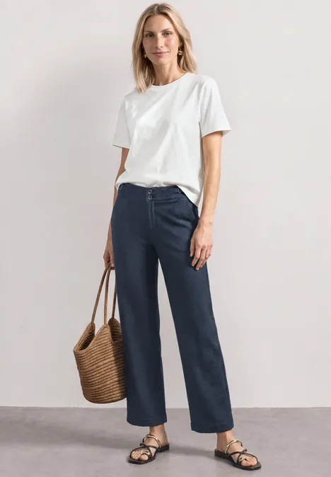 High Waist Jerseybroek met casual pasvorm darkest blue Vrouw in wit T-shirt, marineblauwe wijdvallende jeans, zwarte sandalen en een rieten tas.
