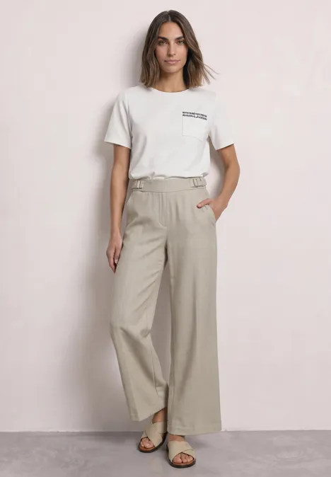 Broek met High Waist en rechte pijpen in casual pasvorm dark creamed sand Vrouw met wit T-shirt, beige wijde broek en sandalen, staand voor een neutrale lichte achtergrond.